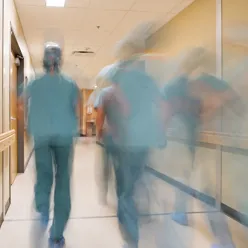 Blury bilde av ansatte i grønne frakker som løper i en sykehuskorridor