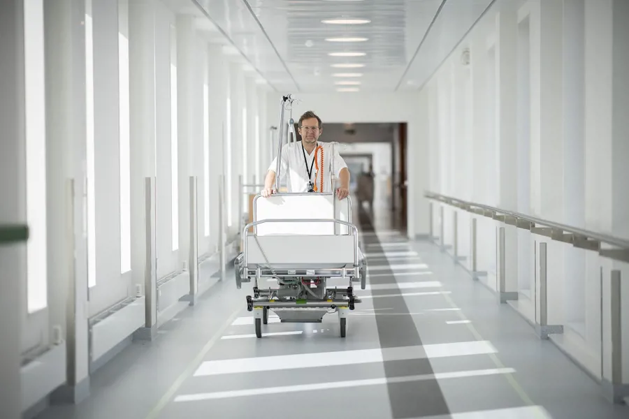 Mannlig portør i hvitt triller tom sykehusseng gjennom korridor