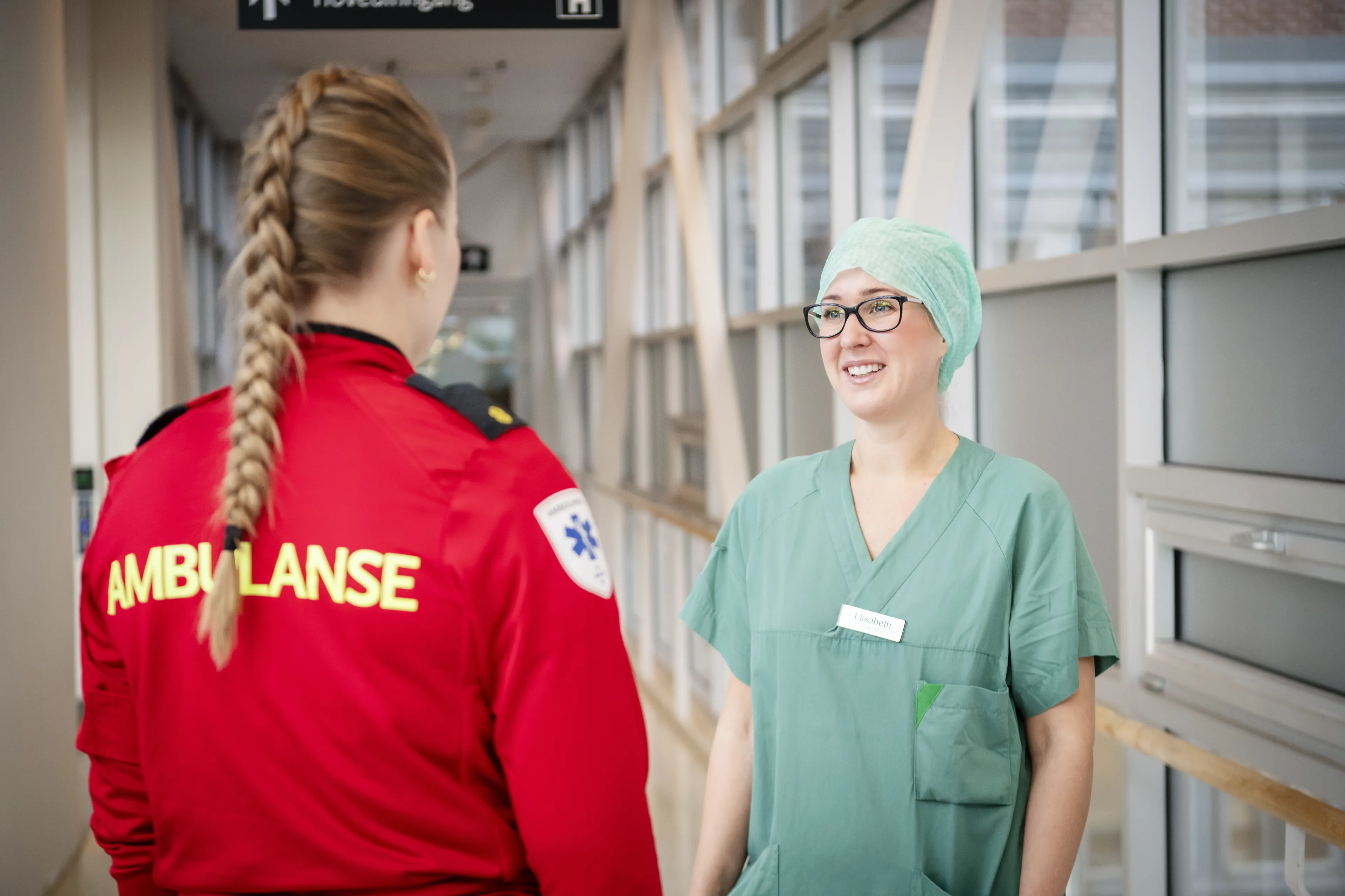 Ambulansearbeider og grønnkledd sykehusansatt kommuniserer i korridor