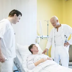 A group of men in white robes standing over a man in a hospital bed