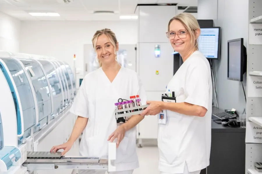 Et par kvinner i hvite labfrakker står i et rom med medisinsk utstyr