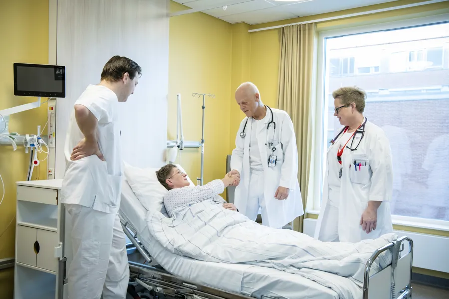 pasient i seng hilser på lege