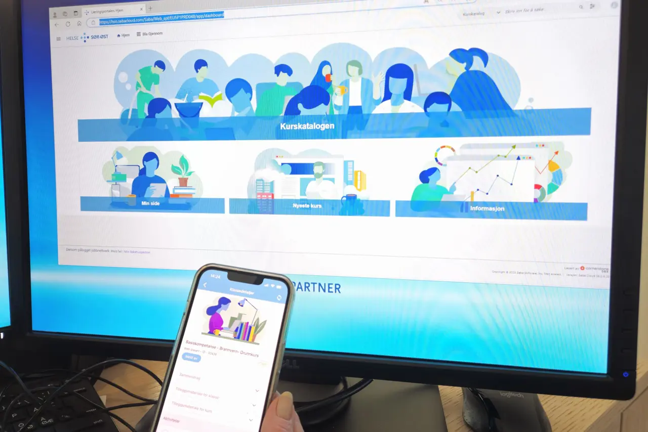 En hånd som holder en telefon foran en dataskjerm