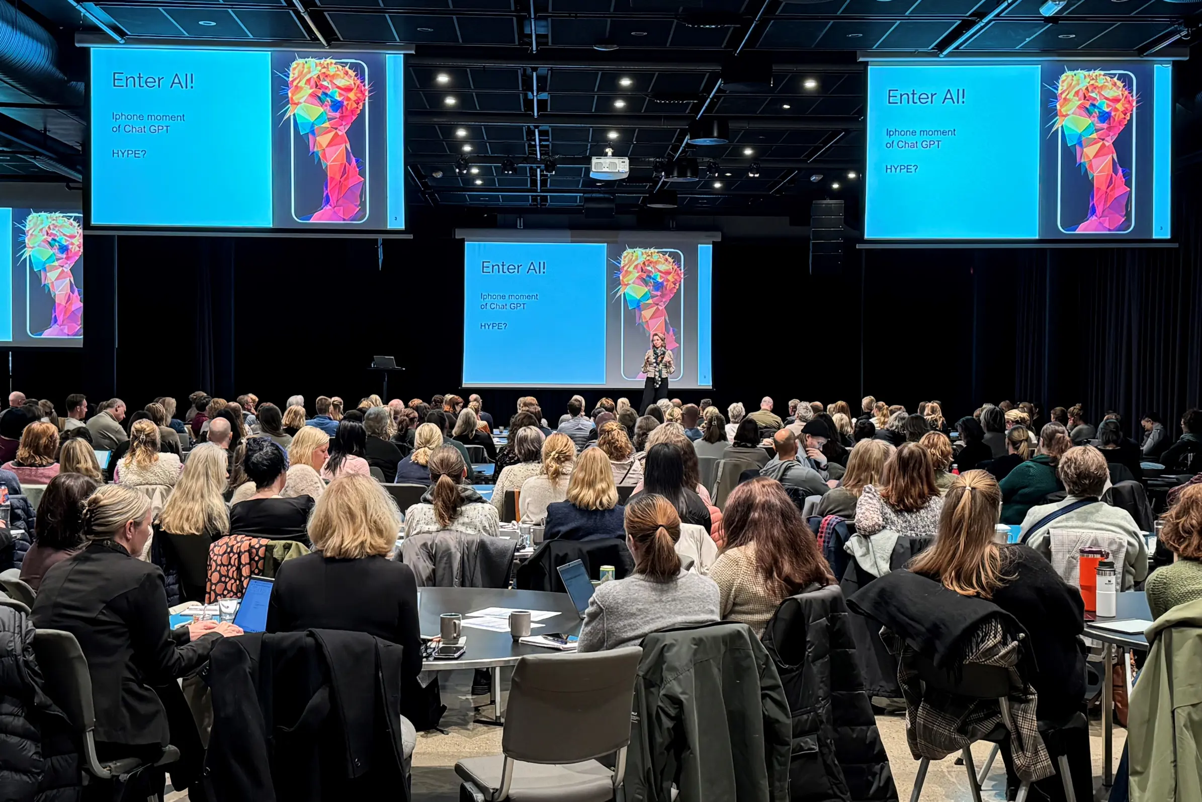 En gruppe mennesker som sitter i et rom med store skjermer